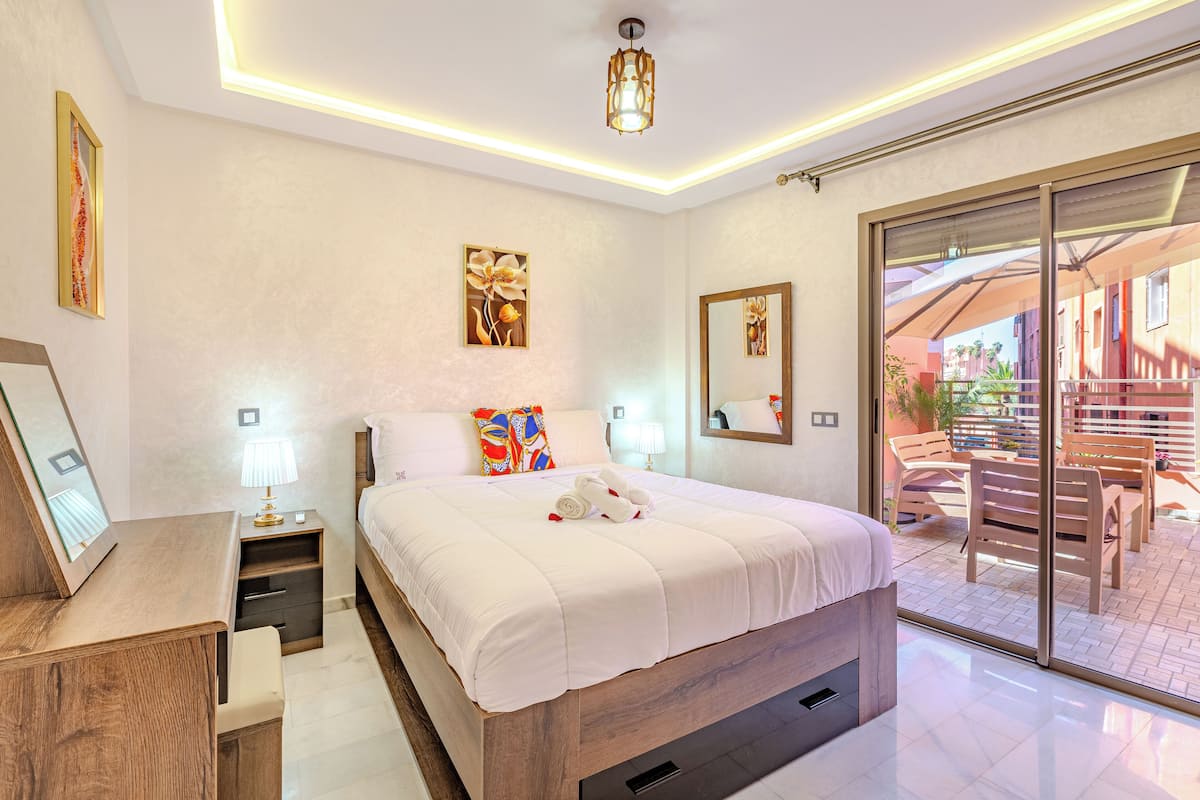 A modern bedroom with a large bed, bedside tables, a desk, and a sliding glass door to an outdoor area.