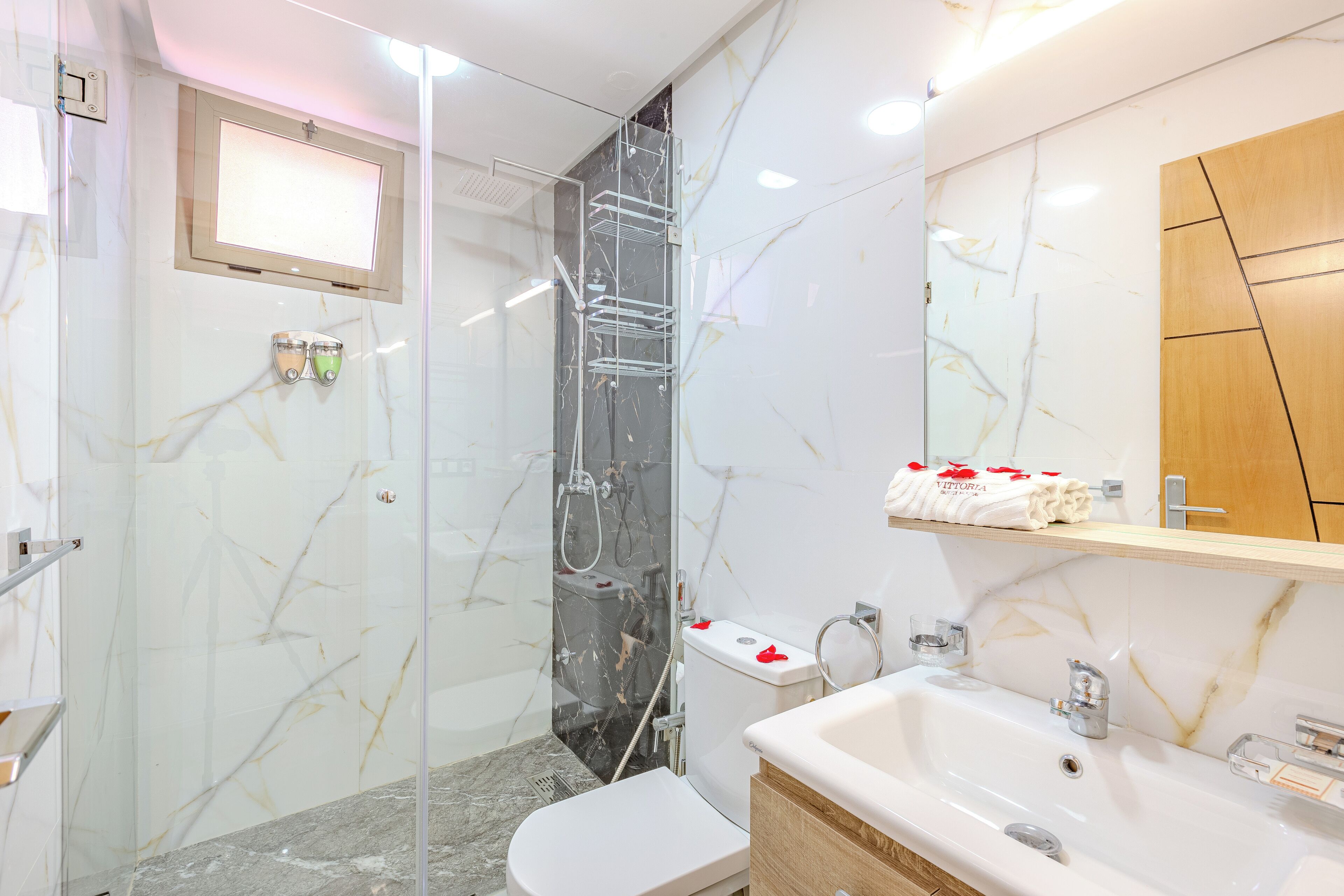 A modern bathroom with a glass-enclosed shower, a white toilet, and a vanity with a mirror and shelf.