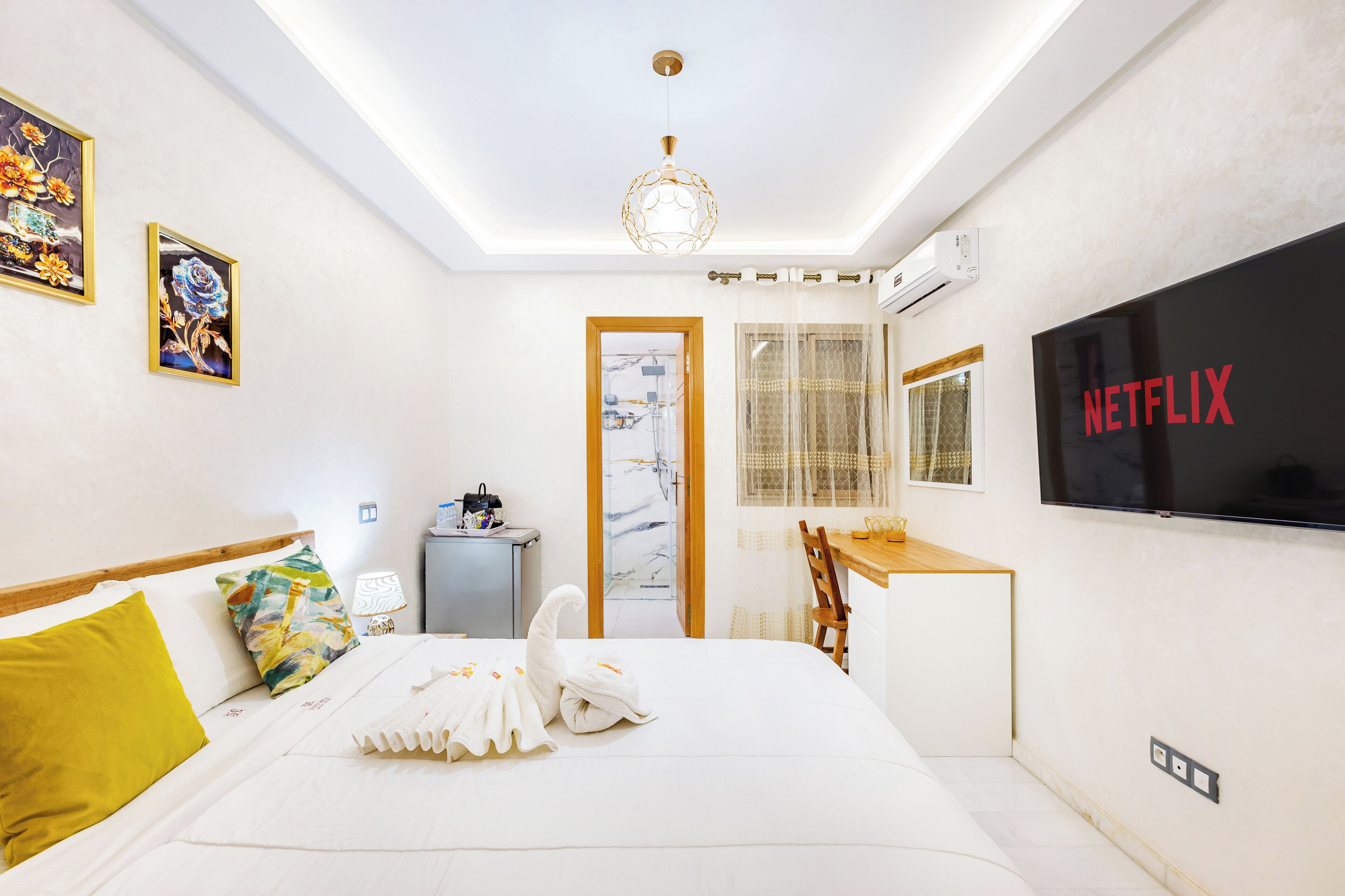 A hotel room with a bed, a desk, a TV, and artwork on the walls.