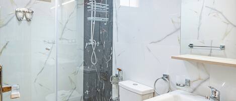 Moderni kylpyhuone, jossa on lasiseinällä varustettu suihku, wc ja peilillä varustettu pesuallas.