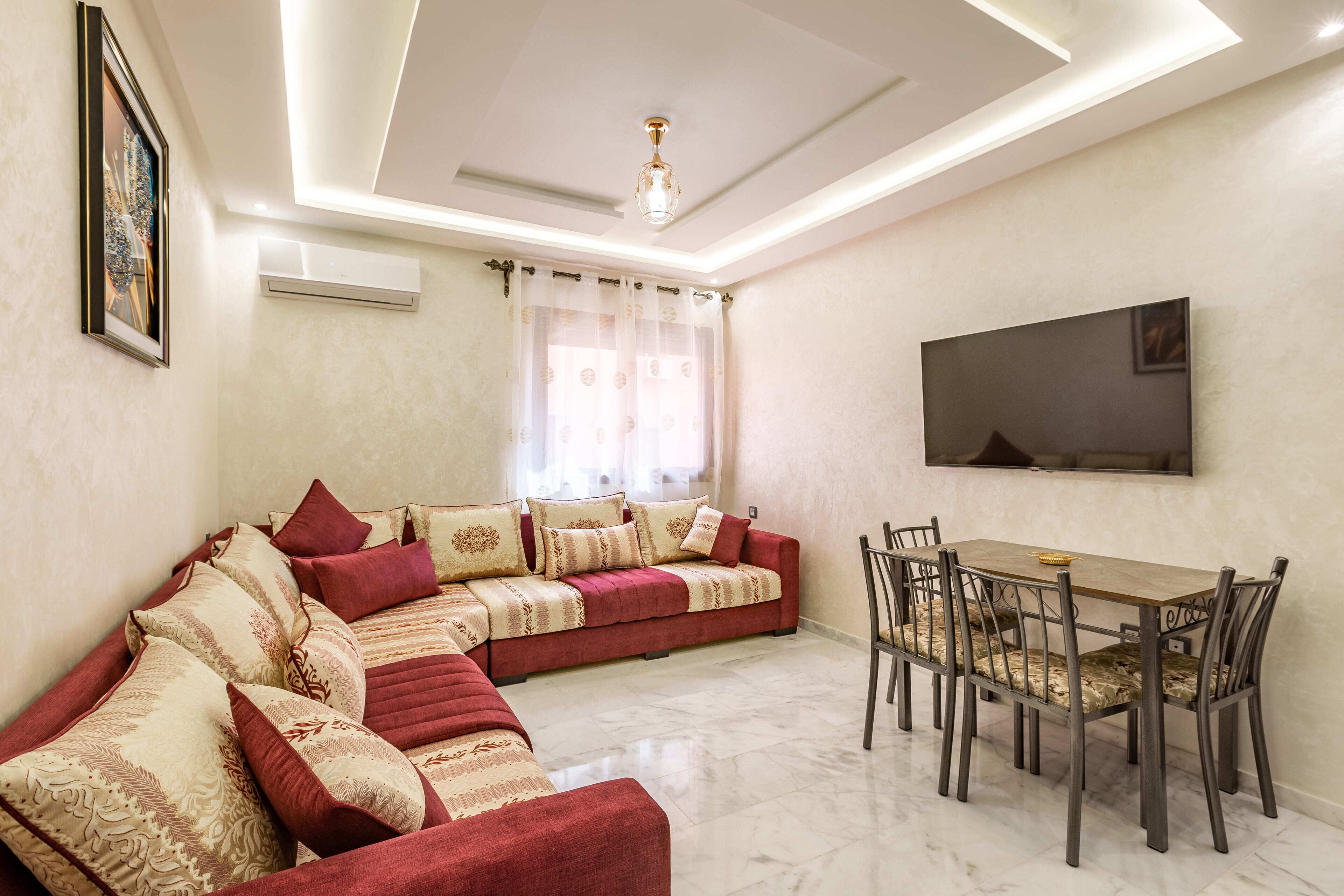 A living room with a sofa, dining table, chairs, and a TV mounted on the wall.