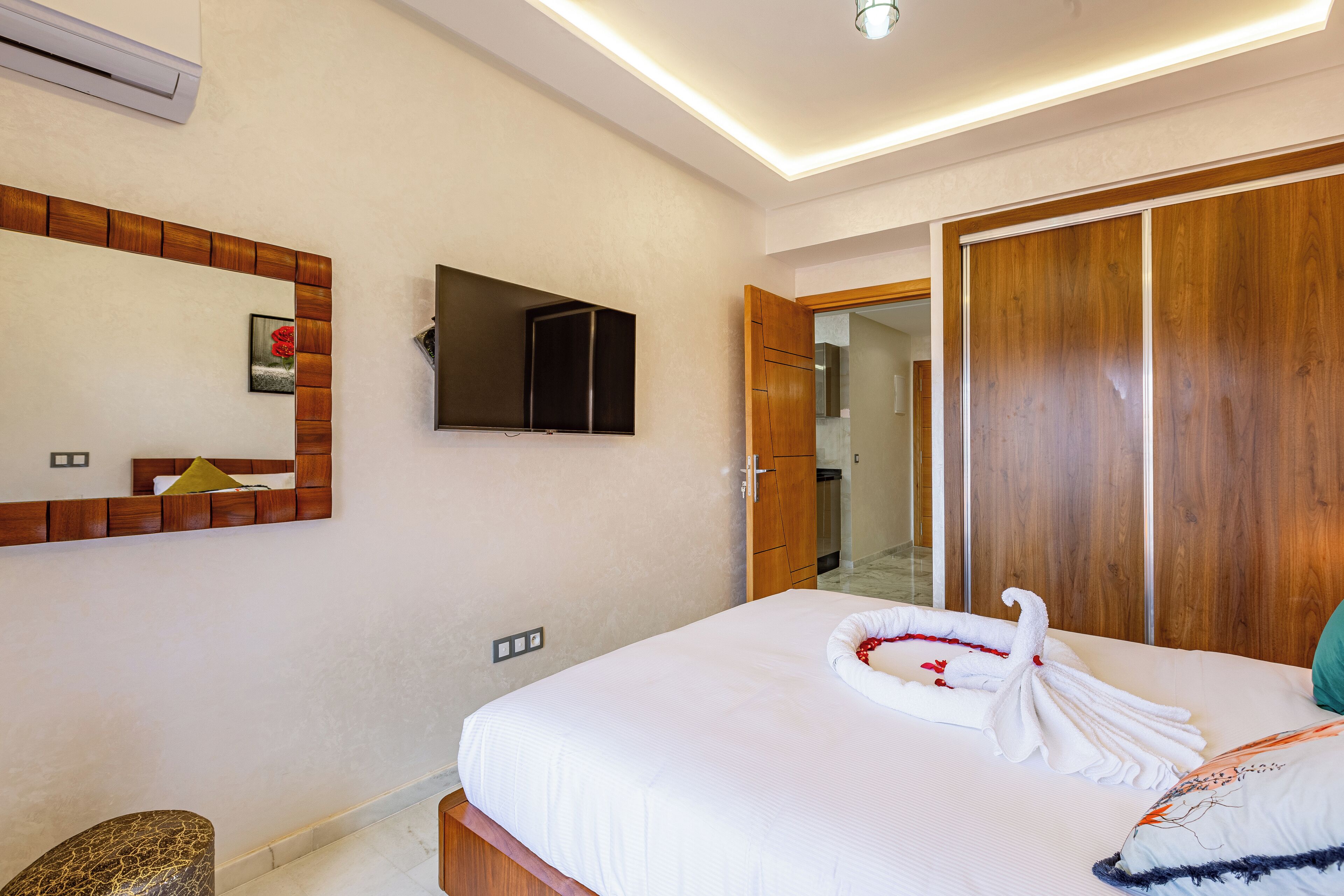 A hotel room with a bed, a wooden wardrobe, a mirror, and a wall-mounted TV.
