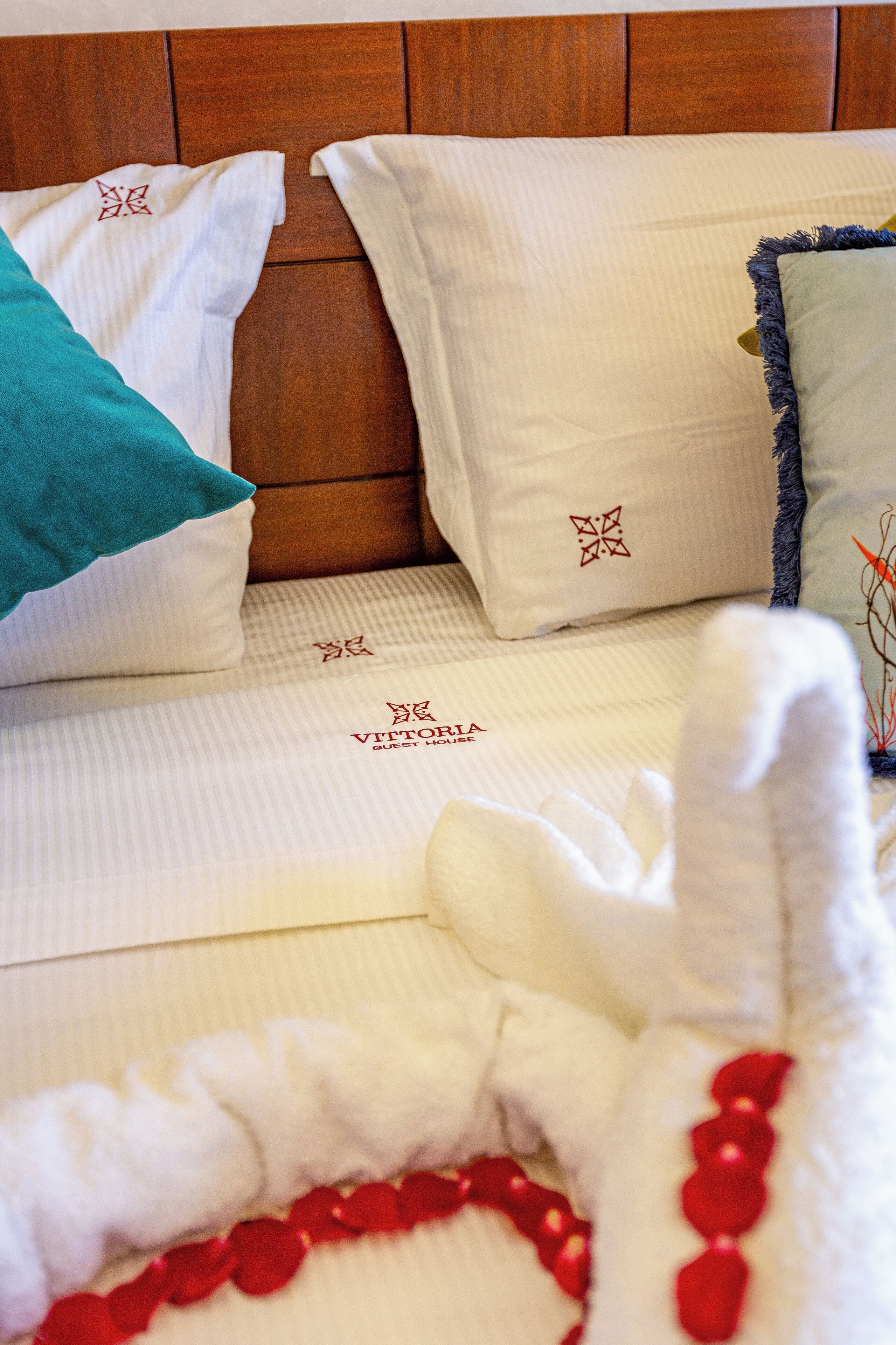A neatly made bed with white linens and decorative pillows, including a teal pillow and a green pillow with a fringe detail.