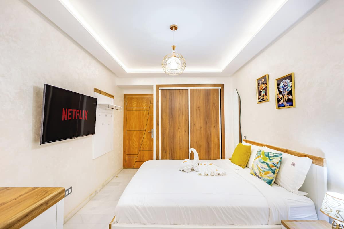 A neatly arranged hotel room with a bed, a TV mounted on the wall, a wooden wardrobe, and a door.