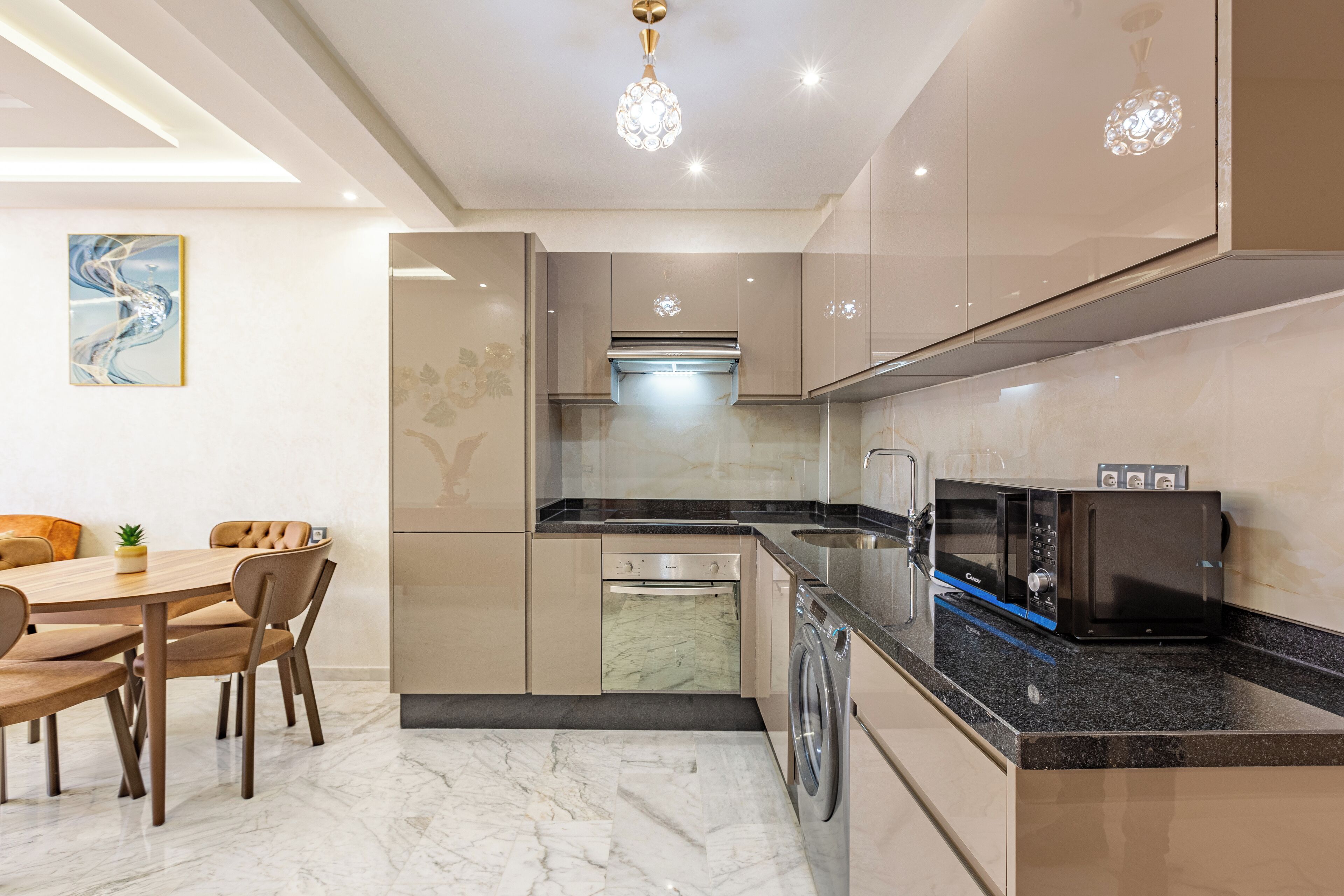 Una cocina moderna con comedor, que cuenta con piso de mármol, electrodomésticos de acero inoxidable y una lámpara colgante.