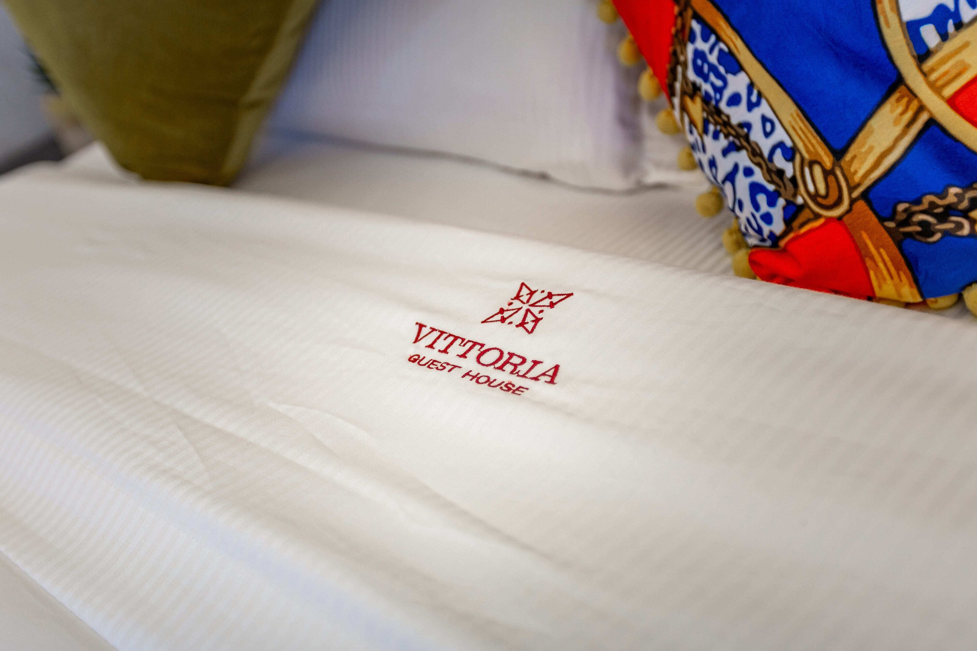 A white fabric with embroidered text reading "VITTORIA GUEST HOUSE".