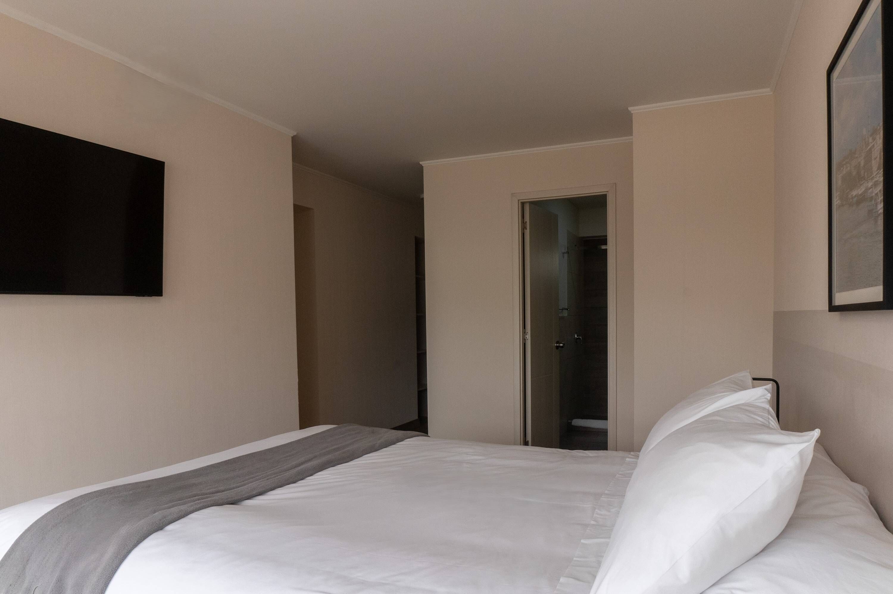 Een hotelkamer met een bed, een flatscreen televisie aan de muur en een deur naar een badkamer.
