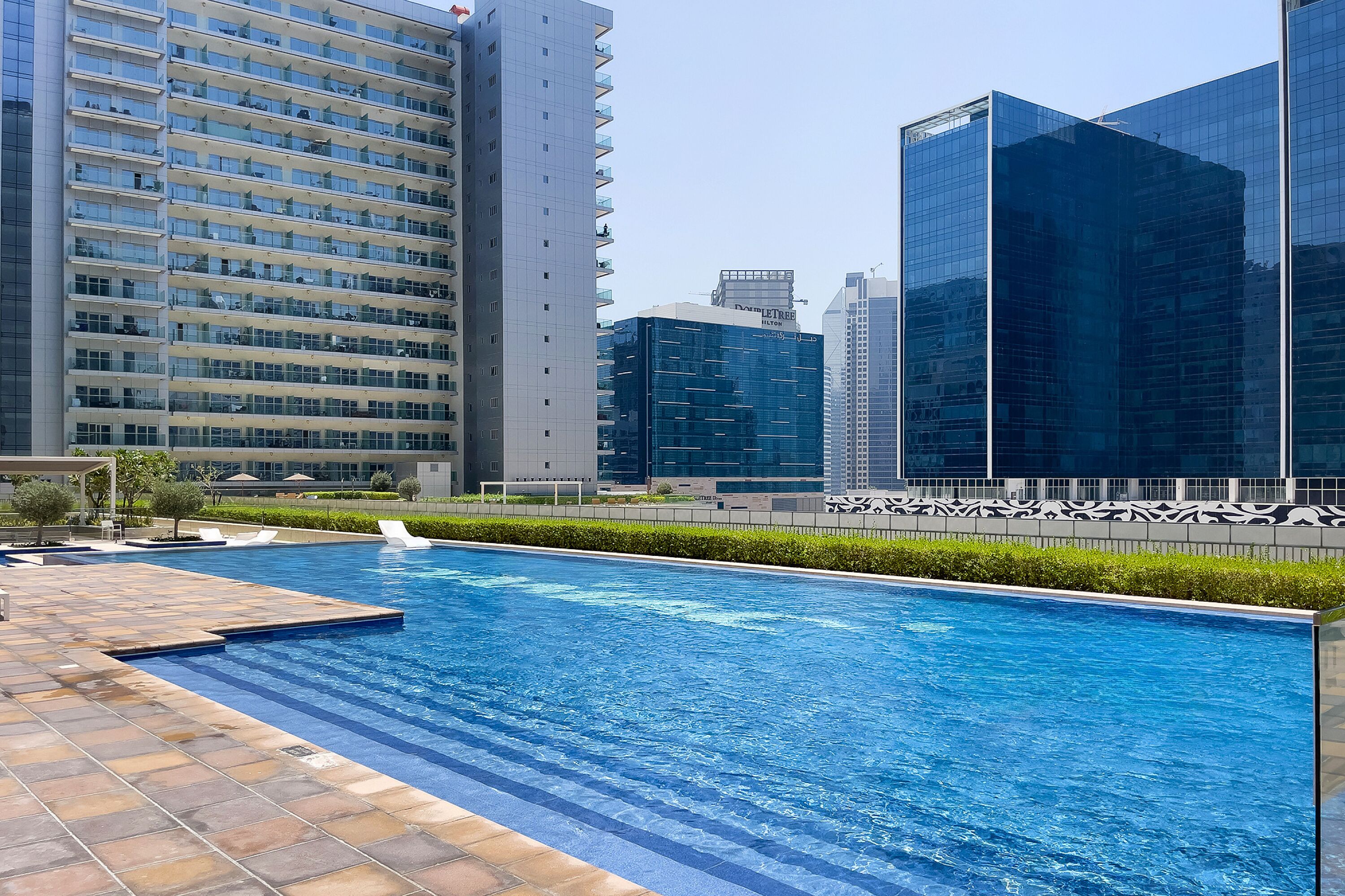 Una piscina con plataforma de baldosas, rodeada de modernos edificios altos.