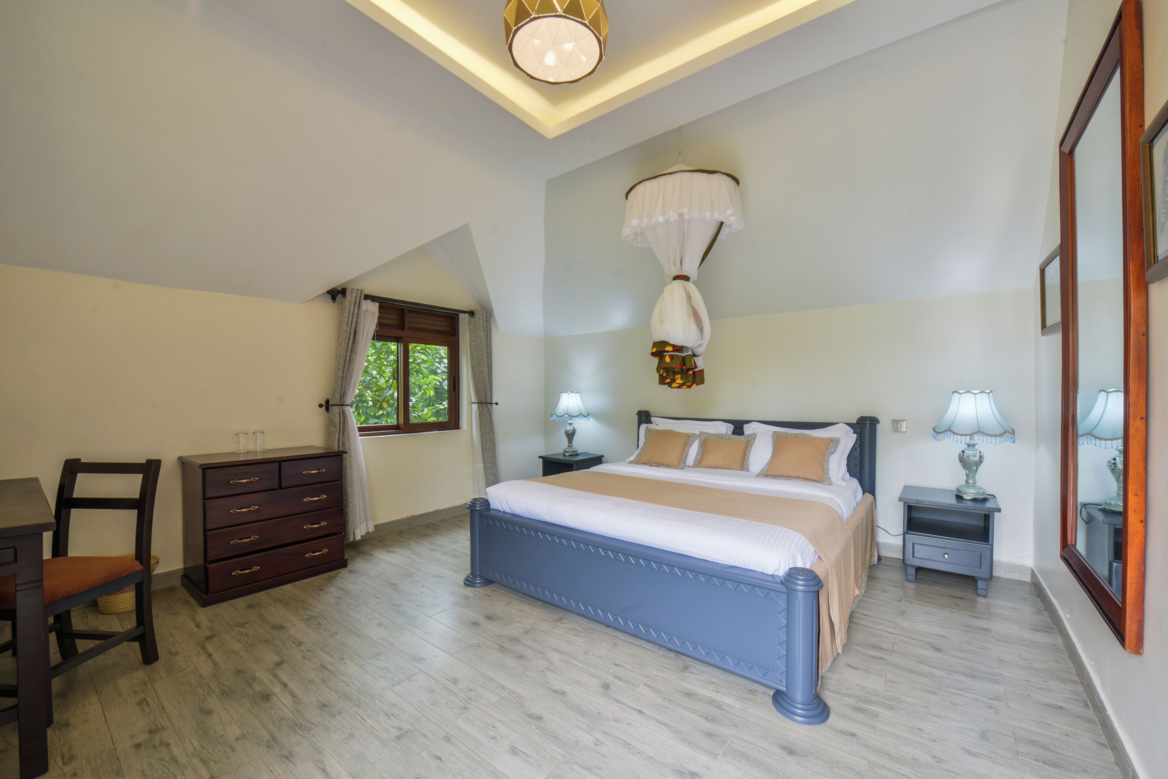 A bedroom with a bed, a desk, a chair, a dresser, a window, and a ceiling light.