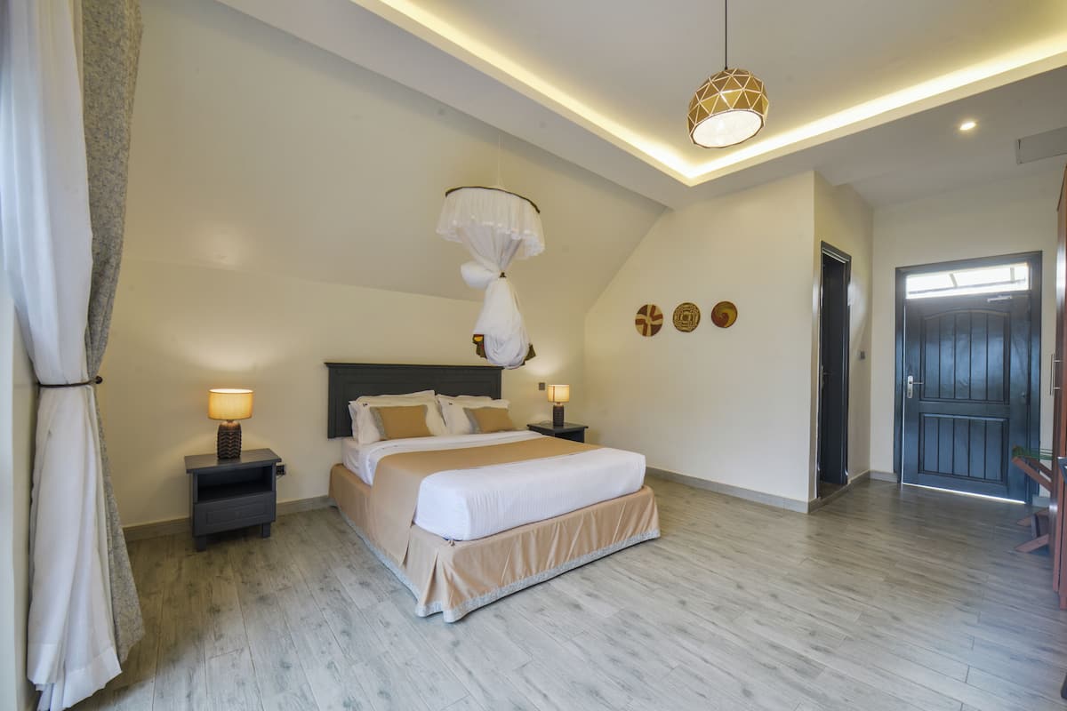 A modern bedroom with a large bed, bedside lamps, a hanging light fixture, and a door with a window.