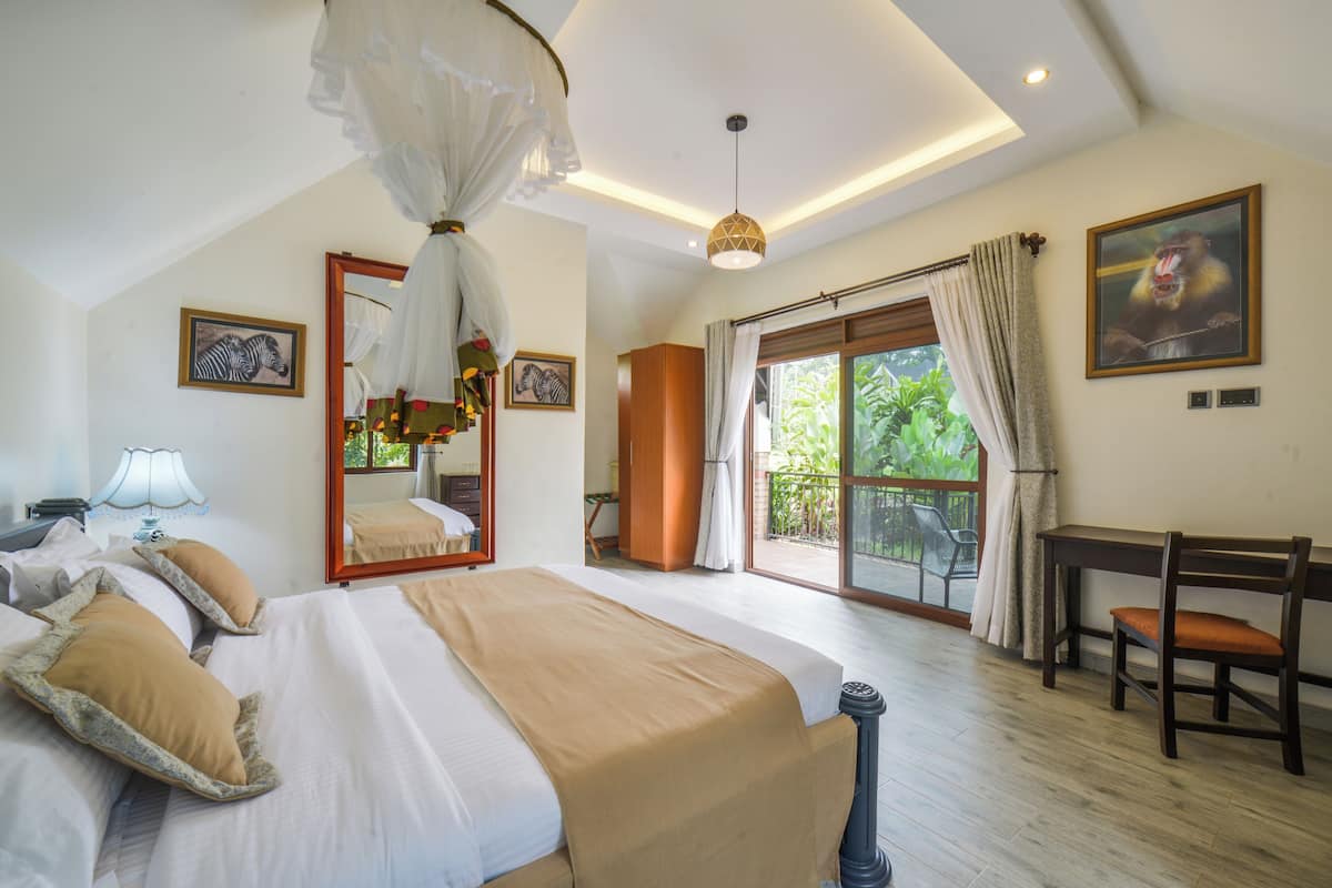 A bedroom with a large bed, a desk, and a view of the outdoors.
