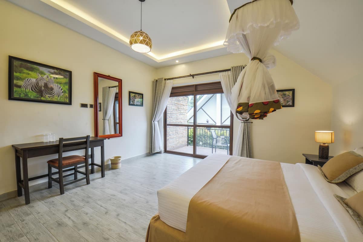 A bedroom with a bed, a desk, a chair, a window with curtains, and a hanging light fixture.