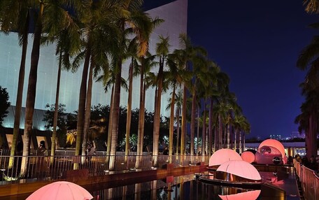 A nighttime view of a waterfront promenade with palm trees and illuminated structures.