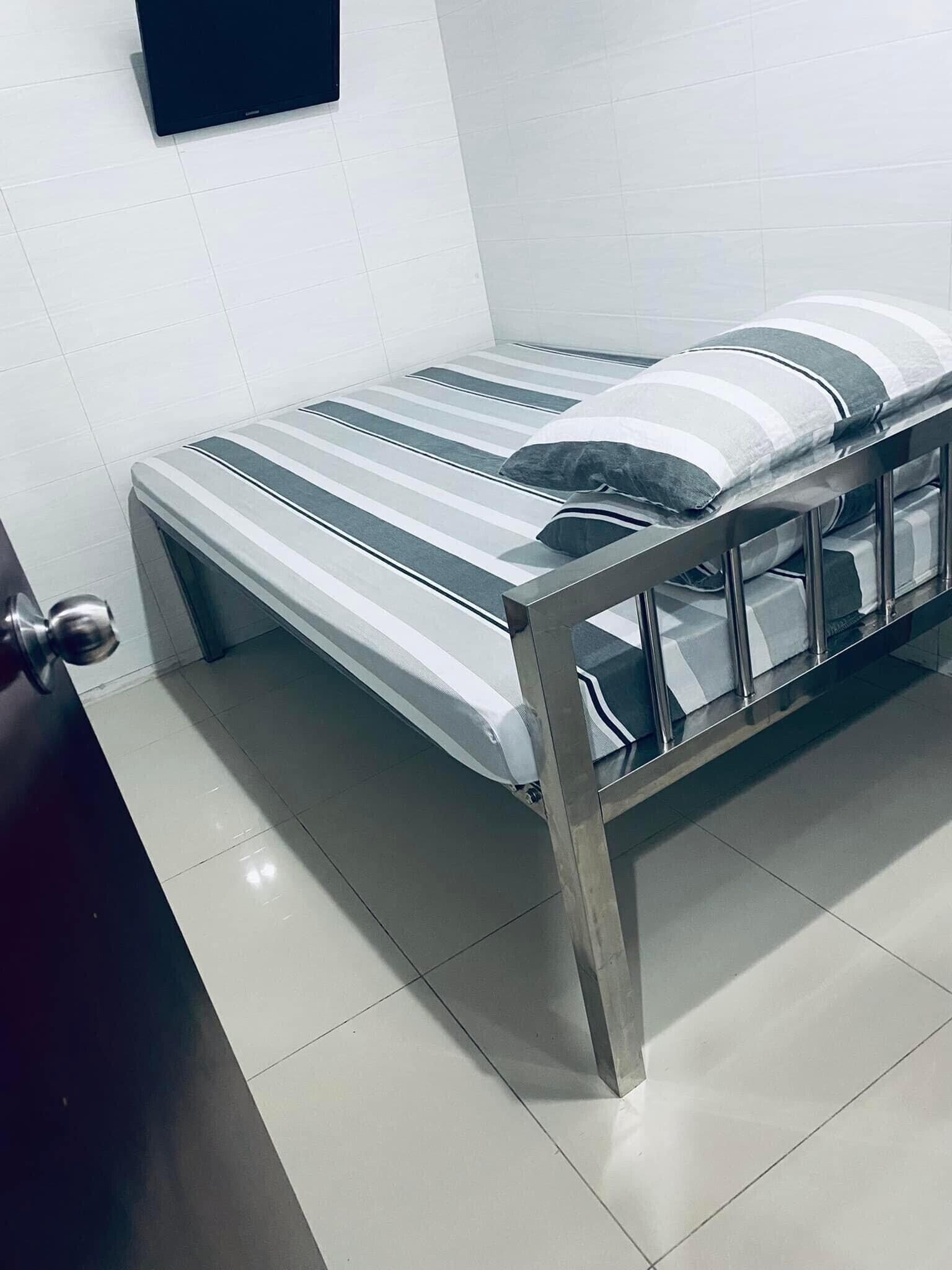 A bed with a metal frame and striped bedding, a flat-screen TV on the wall, and a door with a handle.