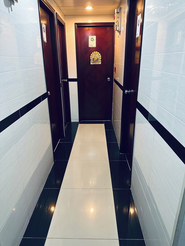 A hallway with a black and white tiled floor, a wooden door with a number, and a small decorative item on the door. - united  co -operate hotel (Kowloon)