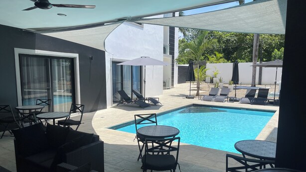 A modern outdoor pool area with lounge chairs, a barbecue grill, and a ceiling fan. - Level Suites #3 Premium Suite (Sosúa)