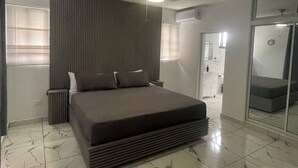 A modern bedroom with a large bed, a ceiling fan, and a bathroom visible through an open door. - Level Suites #3 Premium Suite (Sosúa)