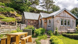 A rustic cabin with a stone foundation and wooden exterior, a wooden picnic table, and a stone pathway leading to the entrance. - The Birdhouse - a luxurious cottage with log burner in the Highlands (Applecross Strathcarron)