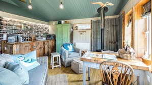 A cozy cabin interior with a rustic kitchen, wooden furniture, and a stone wall backdrop. - The Birdhouse - a luxurious cottage with log burner in the Highlands (Applecross Strathcarron)