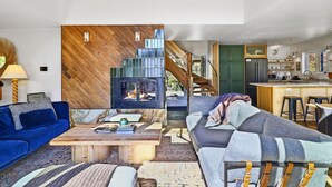 Una sala de estar moderna con chimenea, un sofá, una mesa de centro y una escalera que lleva a una cocina.