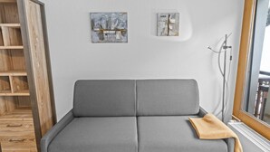Un canapé gris avec un plaid marron, une étagère en bois et deux tableaux abstraits accrochés au mur.