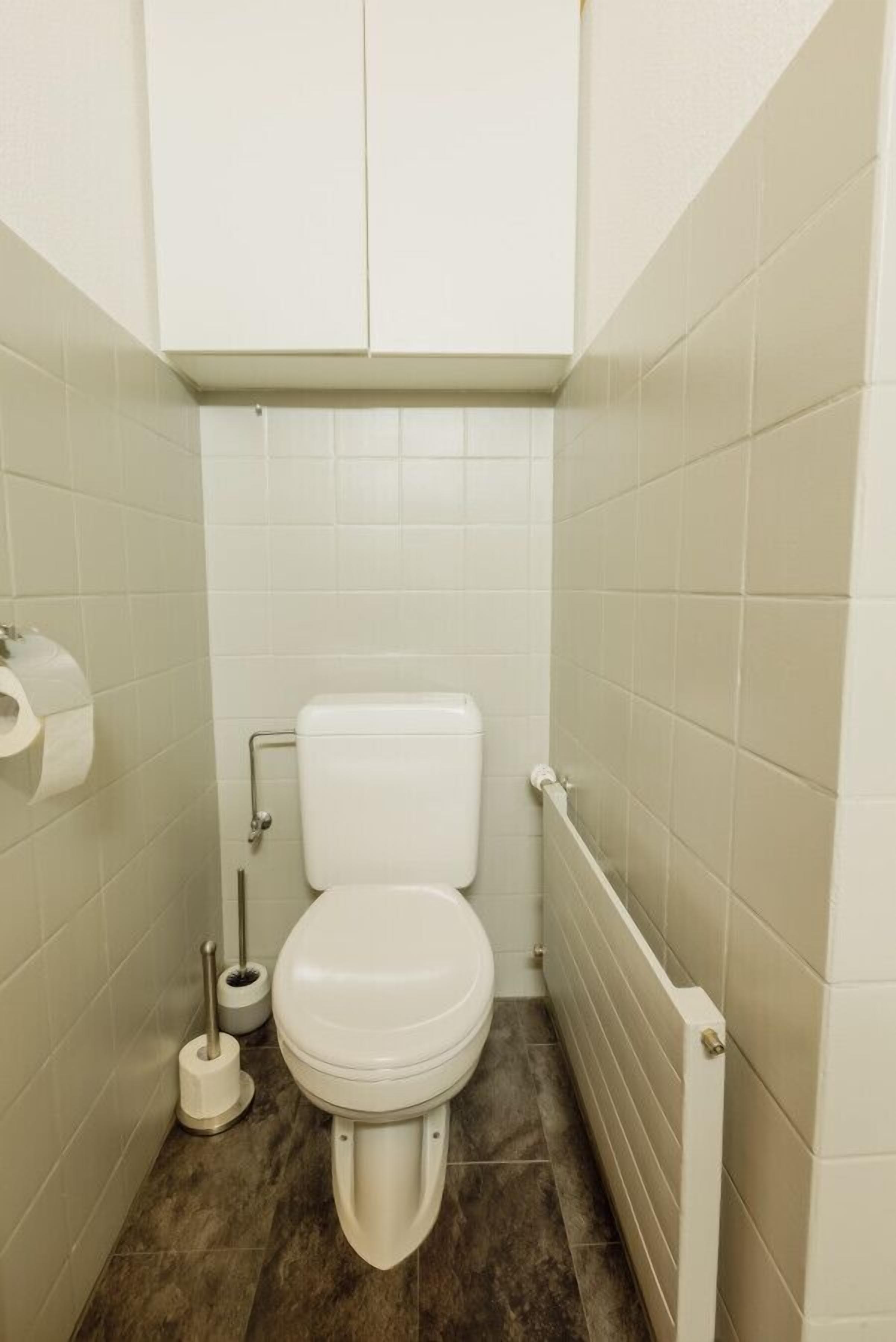 Ein kleines, schmales Badezimmer mit Toilette, Toilettenpapierhalter und einem bodengesteckten Bidet.