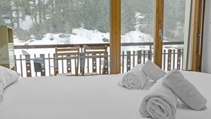 Une chambre d’hôtel avec un lit, deux serviettes enroulées, une rambarde en bois et une vue sur un paysage enneigé.