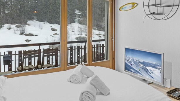 Une chambre avec un lit, une télévision, une fenêtre à cadre en bois et une vue sur un paysage enneigé.