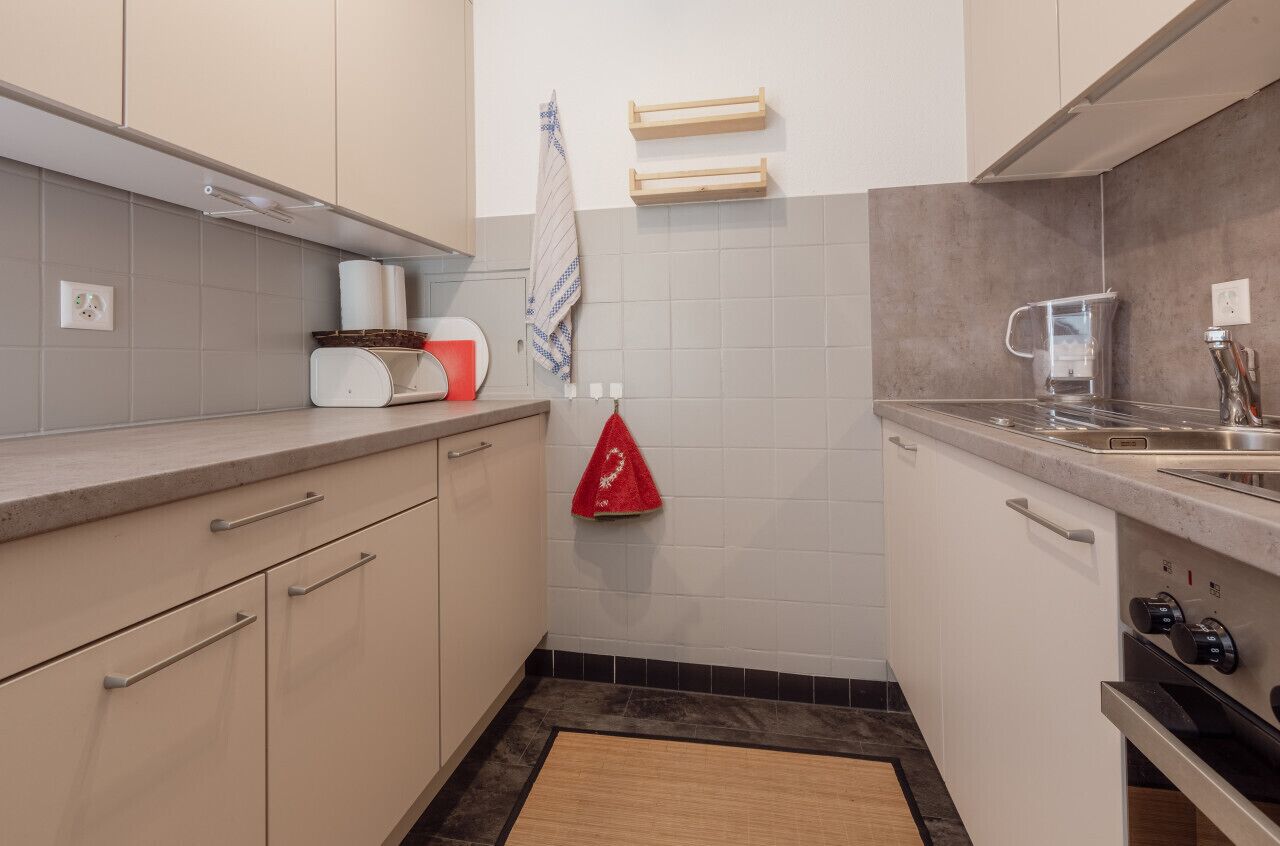 Una cocina compacta con armarios de colores claros, una encimera, un fregadero y una estufa.