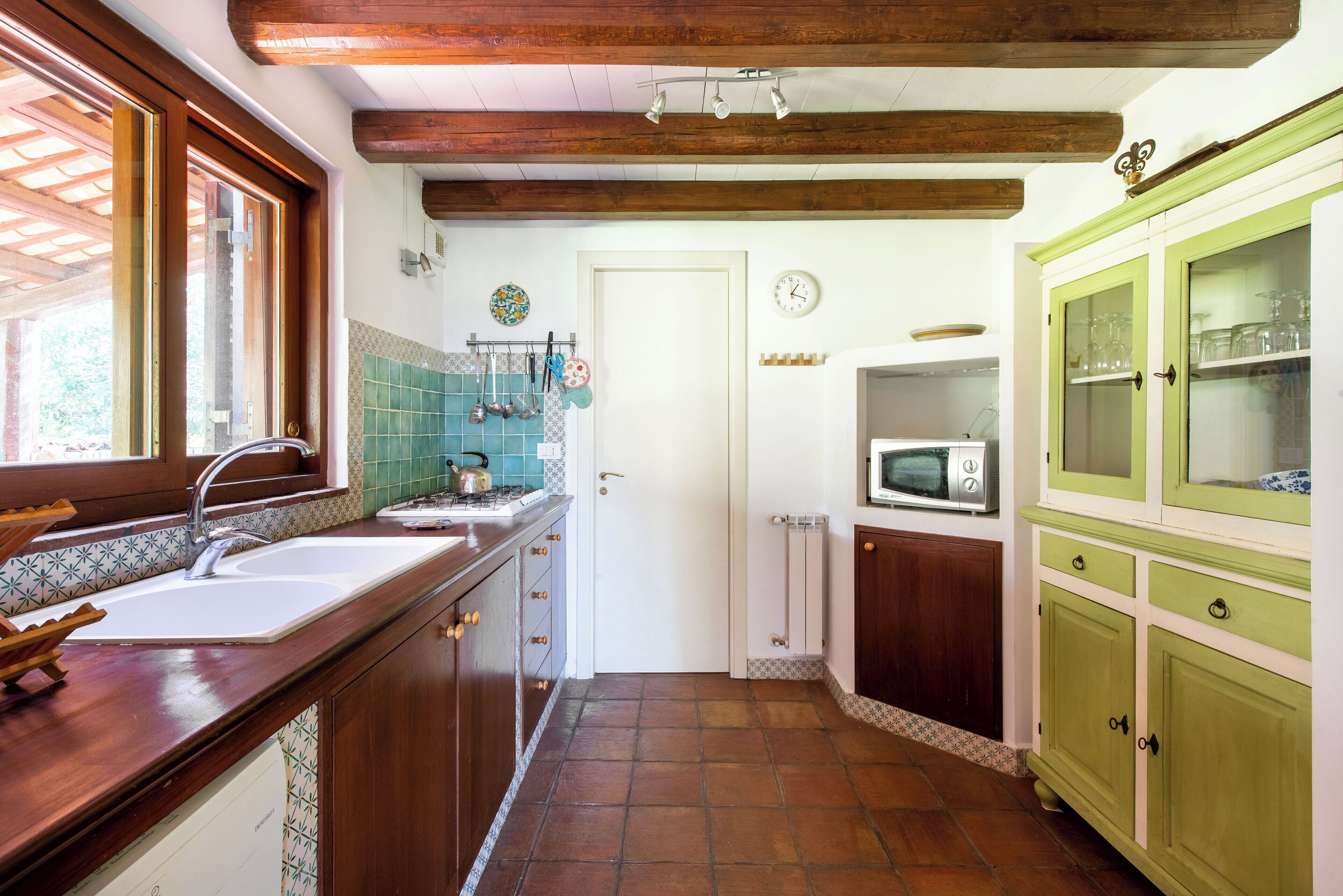 Une cuisine avec un plan de travail en bois, un évier, une cuisinière et un four à micro-ondes. Une porte donne accès à une autre pièce.
