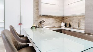 A modern kitchen with a glass dining table, brown leather chairs, and a stainless steel sink.