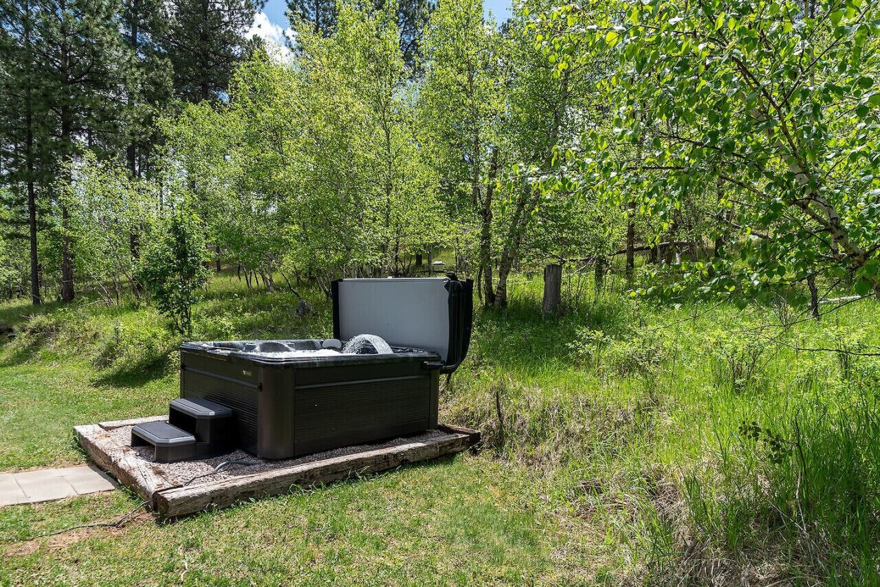 A hot tub in a natural setting with a wooden platform, surrounded by greenery and trees.