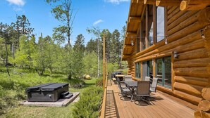 Eine Blockhütte mit einer Terrasse, Sitzgelegenheiten im Freien und einem Whirlpool.