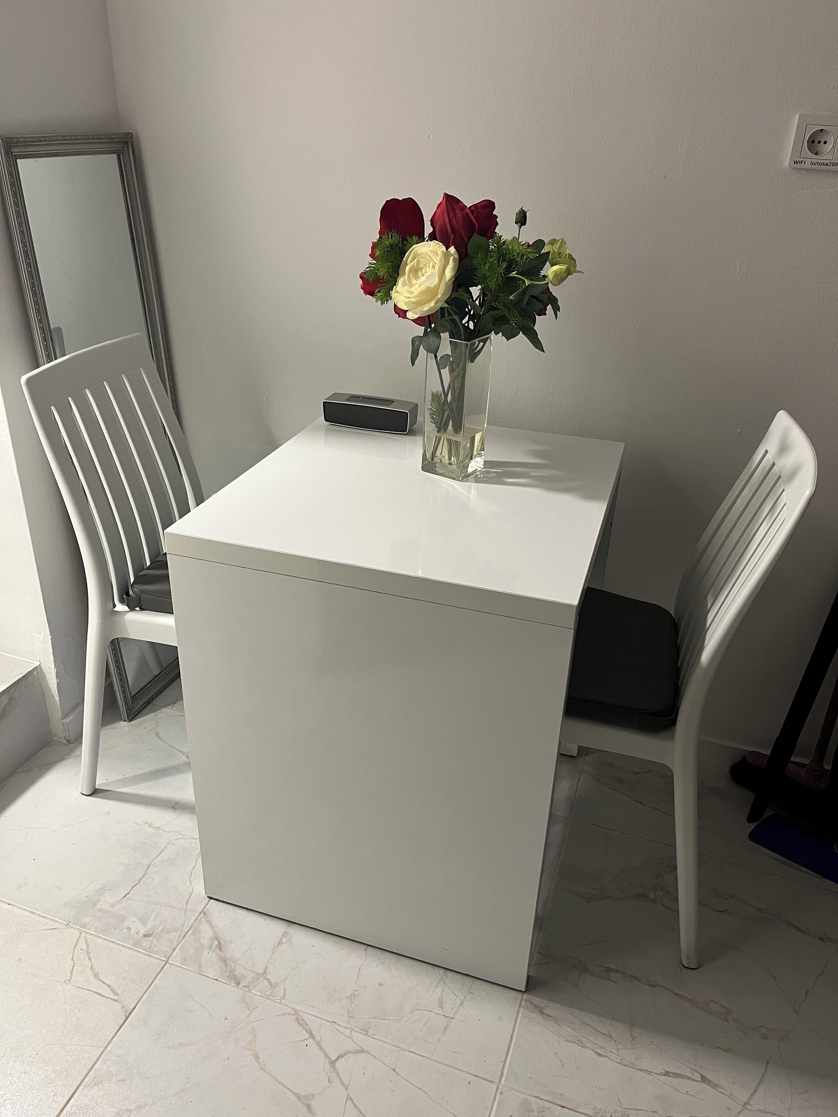 A small, white table with a vase of flowers and a remote control on it.