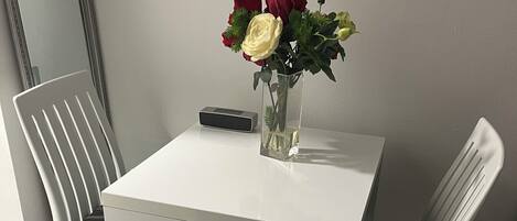 A small, white table with a vase of flowers and a remote control on it.