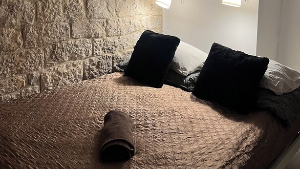 Ein Zimmer mit Steinwand, einem Bett mit zusammengerollter Decke, zwei Wandleuchten und einer Klimaanlage.