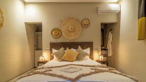 Une chambre avec un grand lit, deux tables de chevet avec des lampes, une tête de lit agrémentée d’une décoration murale et une armoire dont la porte est ornée d’une serviette.