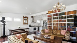 A spacious living room with a large bookshelf, a dining area, and a kitchen.