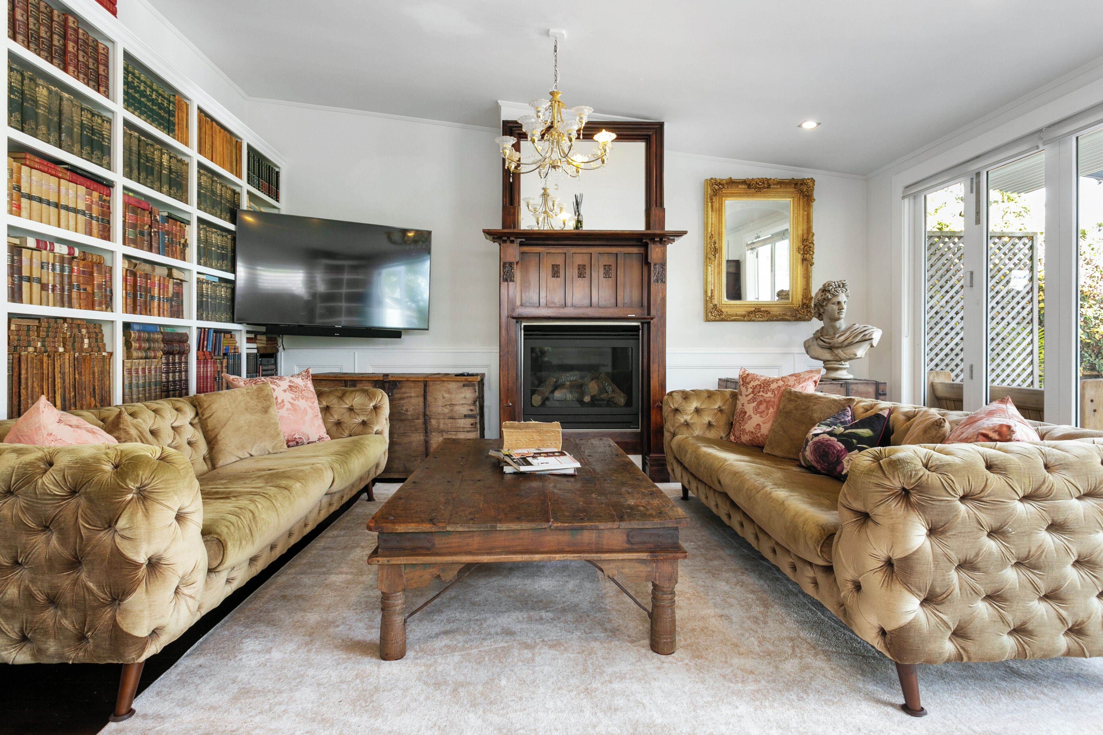 A living room with two tufted sofas, a wooden coffee table, a fireplace, a bookshelf, and a television.