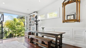 A spacious room with a large window, a wooden bench, a bookshelf, and a mirror.