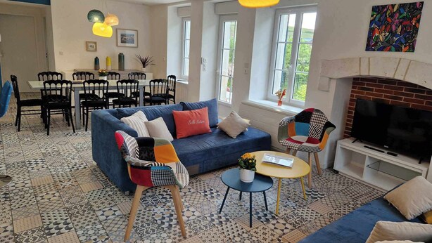 A modern living room with a blue sofa, patterned floor tiles, a fireplace, and a dining area with black chairs and a table.