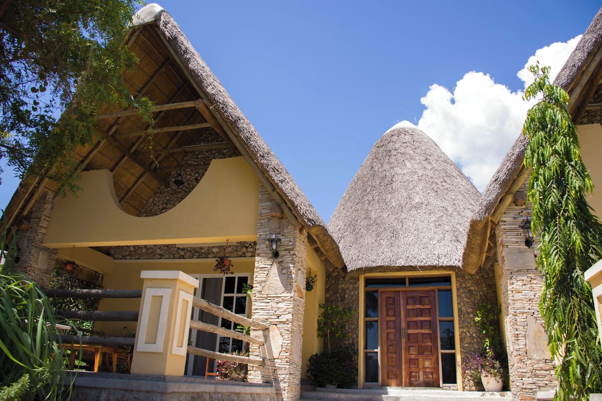 A thatched-roof house with a stone facade, a wooden door, and a staircase leading to a balcony.