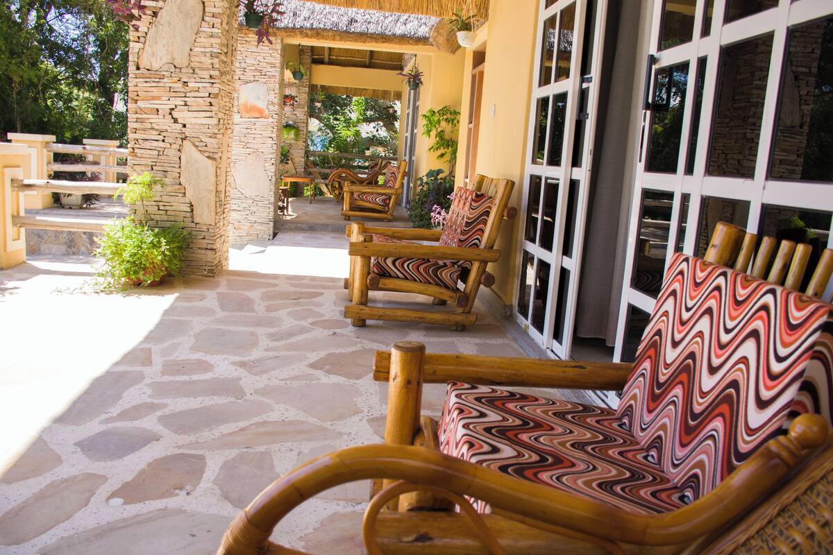 A stone patio with wicker furniture and a thatched roof.