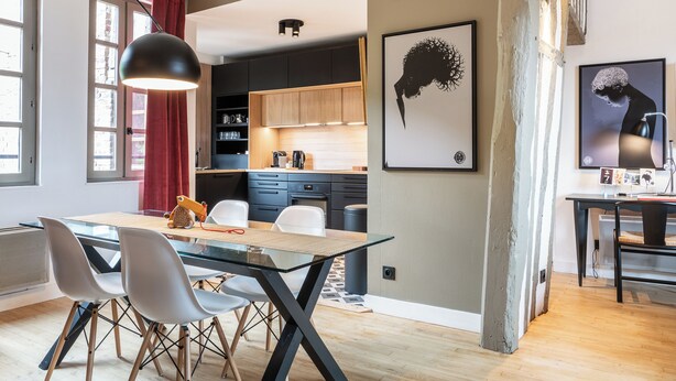 A modern kitchen with dark cabinets, a glass dining table, and a red curtain.