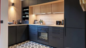A modern kitchen with dark cabinetry, a wooden countertop, and a tiled floor.