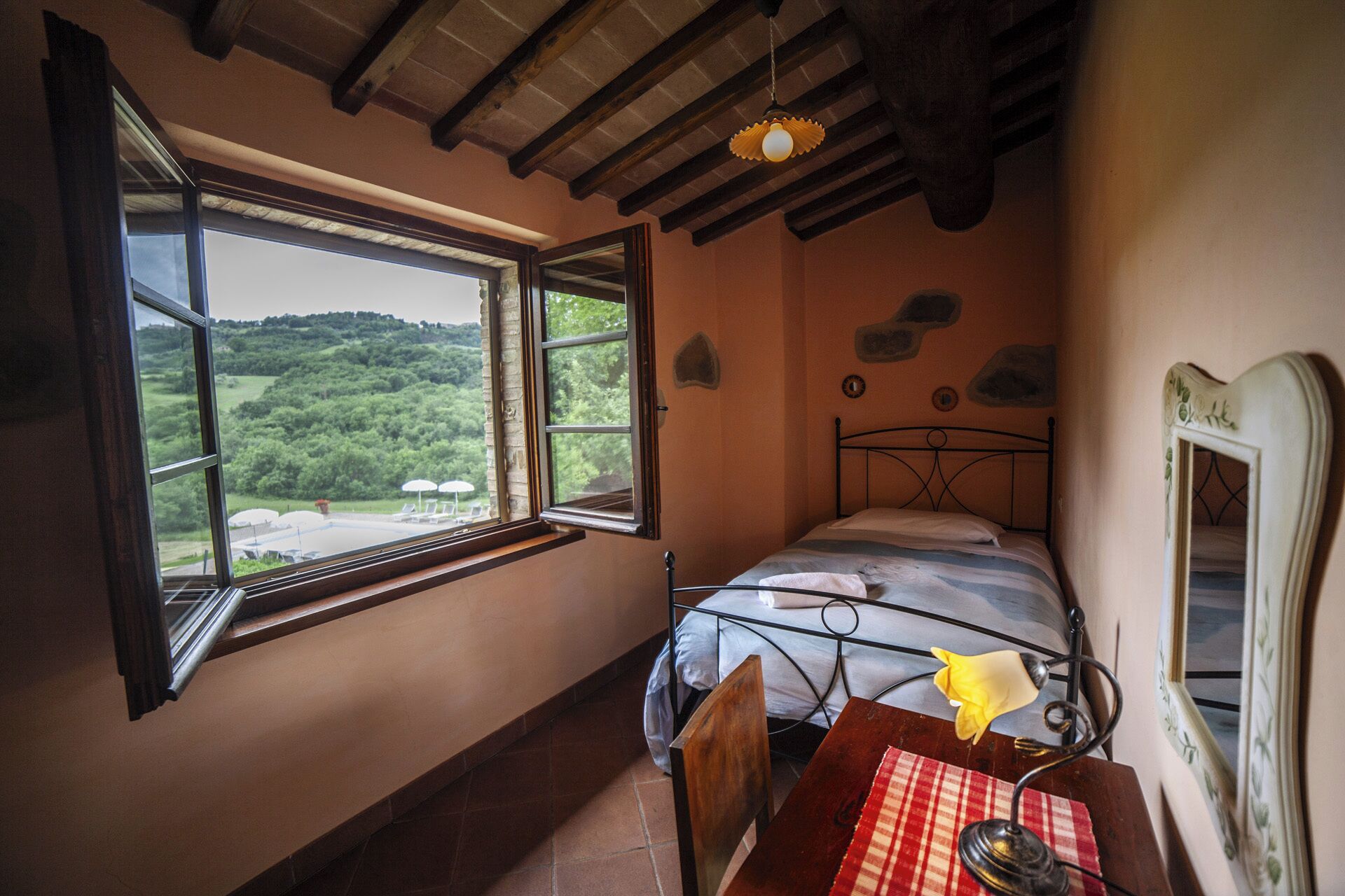 Un dormitorio con cama, una mesa con lámpara, una ventana con vistas a zonas verdes, y un adorno decorativo en la pared.