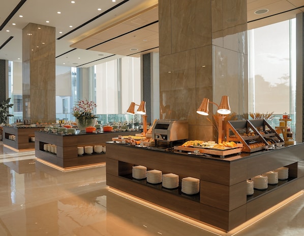 A modern buffet setup with multiple serving stations, a polished floor, and large windows allowing natural light. - Centre Point Danang Hotel & Residence (Da Nang)