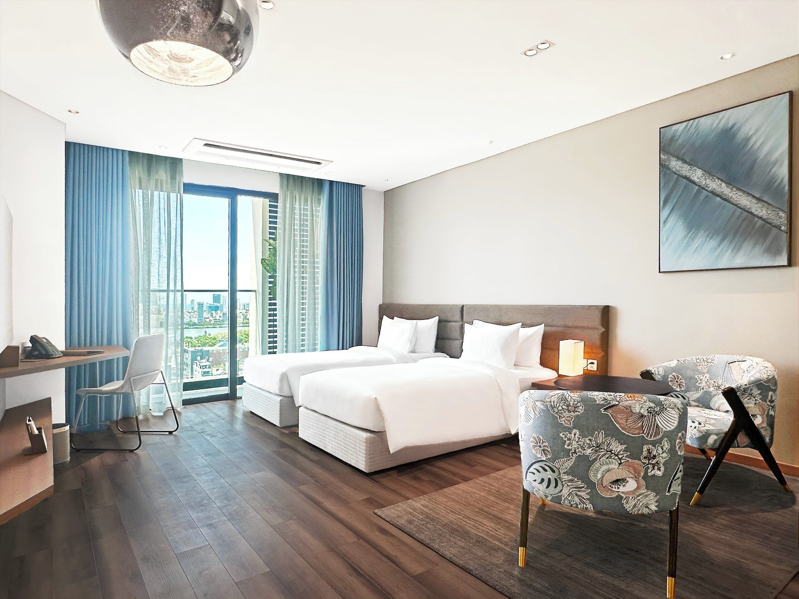 A hotel room with a large bed, a desk, a chair, and a view of the city.