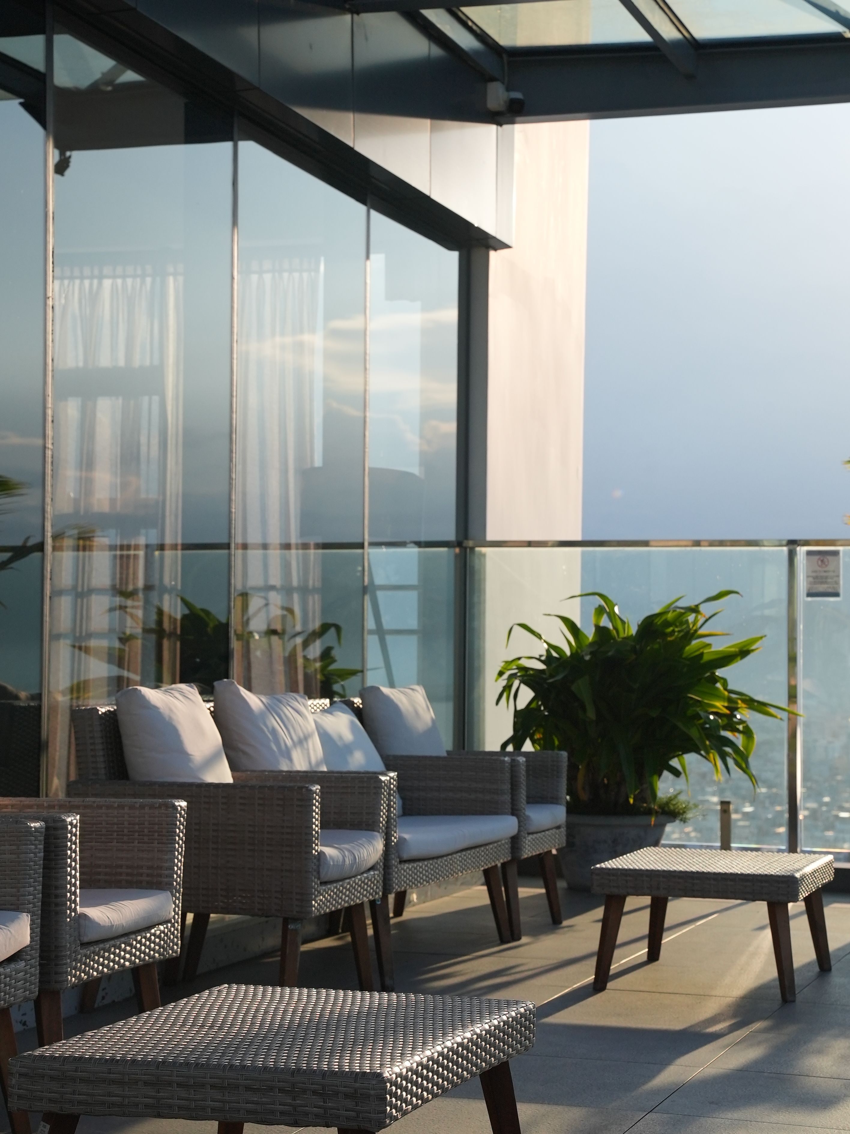 Een balkon met rieten meubilair, een potplant en uitzicht op de stad.