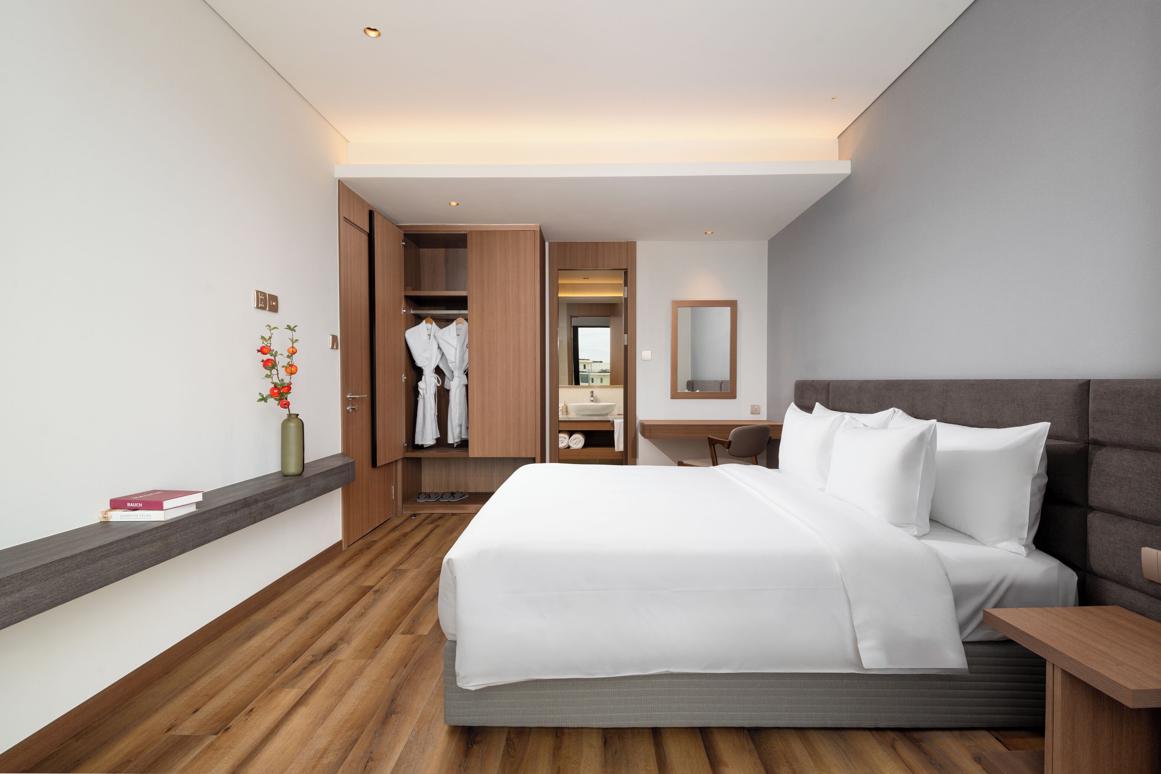 A hotel room with a bed, bedside table, a mirror, a desk, a wardrobe, and a small bathroom.